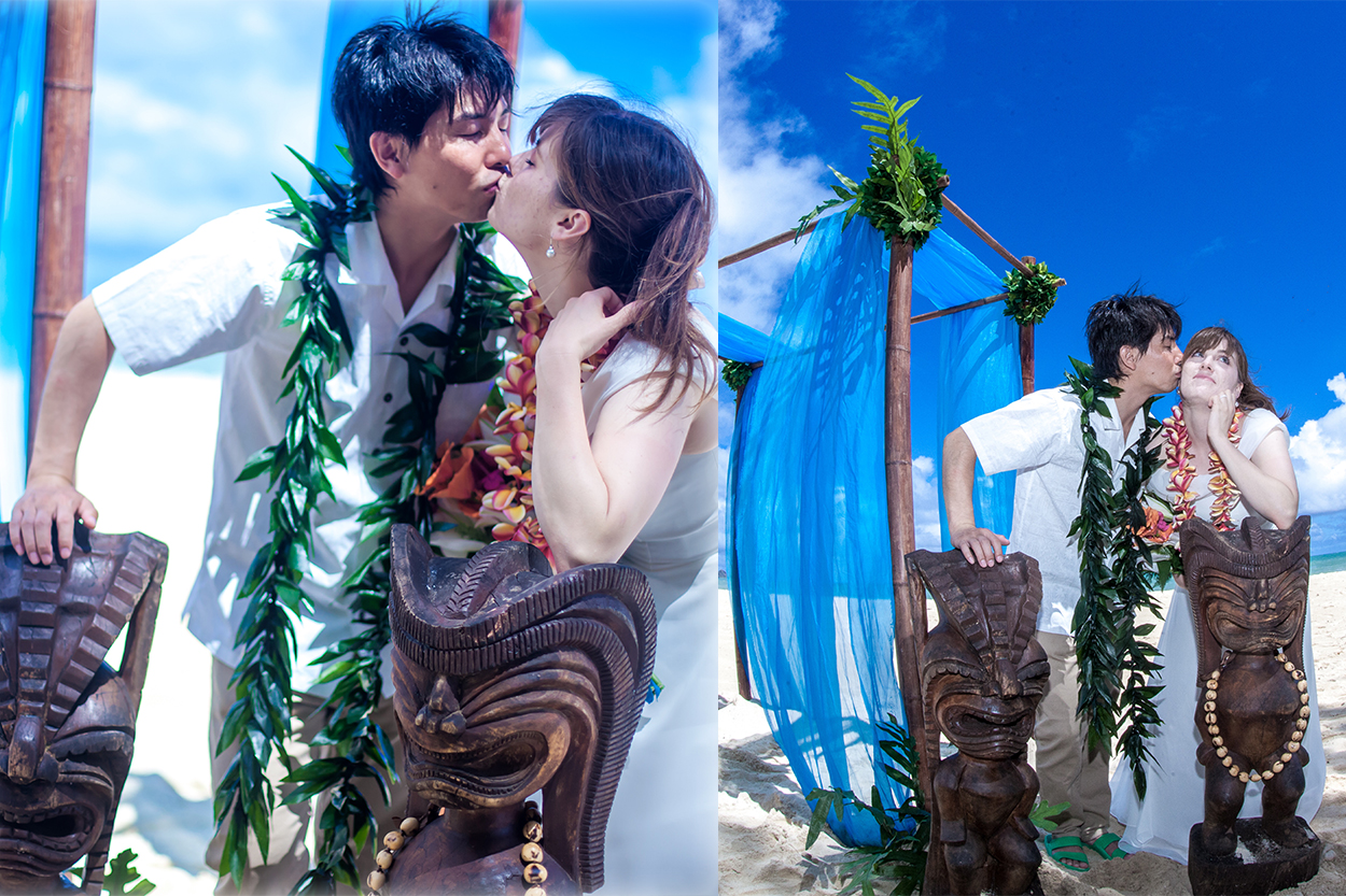 Couple kissing beside carved tiki statues and blue drapes on the beach